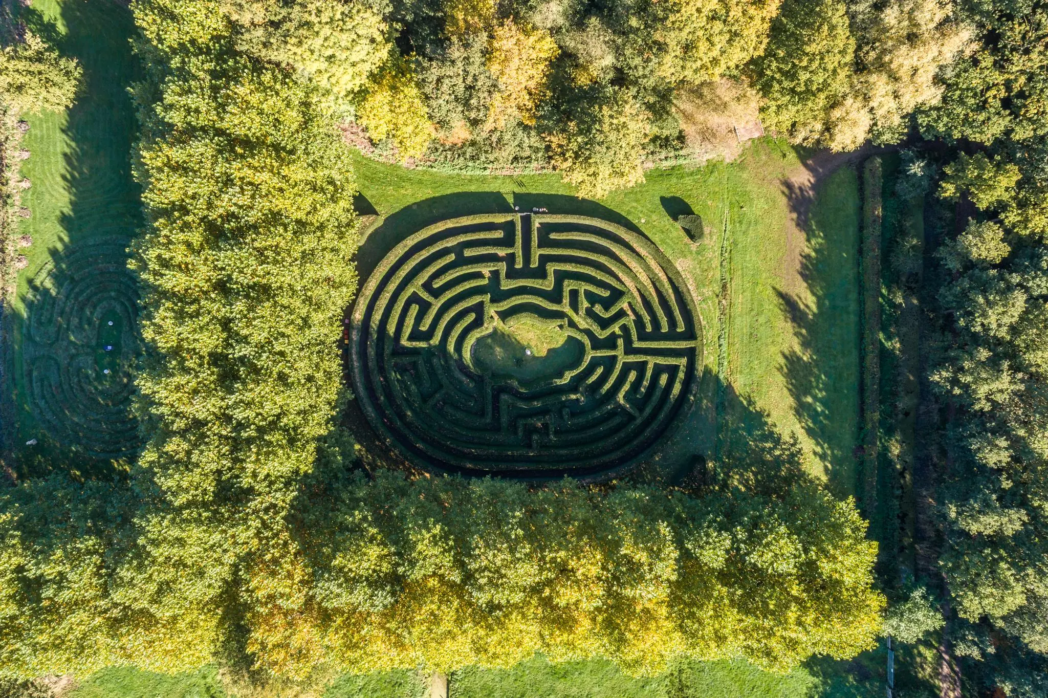 Luchtfoto van een doolhof in het groen aan de Langbroekerdijk, omringd door bomen en grasvelden.